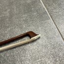 Detailní pohled na hmatník smyčcového nástroje s bílým pražcem. Hmatník je vyroben z tmavě hnědého dřeva s viditelnou strukturou slásek. Přes něj jso…