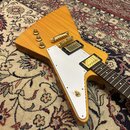 Elektrická kytara s žlutým trupem ve tvaru šipky a bílým pickguardem. Nástroj má zlatý hardware, dva humbuckery a tři ovládací knoflíky. Hmatník je t…