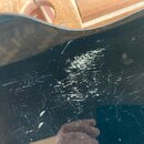 Detailní záběr na černý lakovaný povrch hudebního nástroje. Povrch vykazuje výrazné opotřebení v podobě četných škrábanců a rozsáhlého odřeného místa…