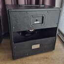 Zadní strana černého kytarového komba s povrchem z texturovaného vinylu. V horní části je vstupní panel s nápisem INPUT a štítkem, na kterém je čárov…