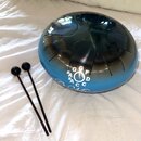 Modro-stříbrný kovový steel tongue drum s vyfrézovanými jazyčky. Na povrchu je bílý nápis s označením tónů G, F, D, A, C, C a značky # u některých pí…