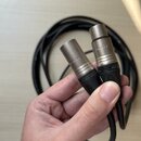 Černý audio kabel s dvěma konektory typu XLR. Na kovových částech konektorů je vyražen nápis „xx-au“ a na černých plastových krytech je vidět značka…