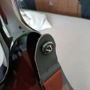 Detail zadní strany tmavě červené elektrické kytary s lesklým povrchem. Na korpusu je upevněn hnědý kožený řemen s textilním popruhem. Řemen je přich…
