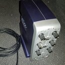 Tmavě modré zařízení s šedým předním panelem a černými ovratovými knoflíky. Na horní části panelu je nápis LAMBDA a pod ním popisky Mic 1 Peak, Mic 2…