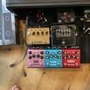 Sestava efektů na černém pedalboardu. V horní části jsou pedály s nápisy OCTAPUS I a Cali76 Origin Effects. Uprostřed je zlatý pedál Ja Granger s ovl…