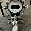 Elektronický basový pedál s černým korpusem a bílým plochým povrchem. Na horním okrače je nápis Roland a pod ním Head made by REMO, uprostřed povrchu…