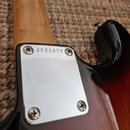 Detail krku a spoje s tělem elektrické kytary v sunburst provedení. Na kovém spojovacím plechu je vyražen nápis JV32679. Povrch plechu vykazuje drobn…