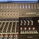 Fotografie zachycuje část míchacího pultu s nápisem AUDIENT ASP 4816 HERITAGE EDITION. Zařízení má šedý kovový povrch a je vybaveno řadou posuvníků,…
