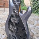 Elektrická basová kytara s tmavě šedým metalizovaným povrchem a černým pickguardem. Nástroj má dva snímače typu humbucker a čtyři černé oválné ovláda…