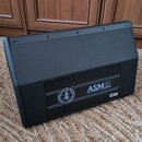Černý aktivní stage monitor s hranatým tvarem a matným povrchem. Na zadním panelu je nápis ASM10 ACTIVE COAXIAL STAGE MONITOR a kulaté logo s textem…