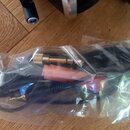 Černý audio kabel s pozlacenými konektory, umístěný v průhledném plastovém sáčku. V sáčku se nachází rovněž růžový pěnový kryt na mikrofon. Na kabelu…
