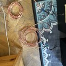 Na dřevěné podlaze a modrém koberci leží dva svazky tenkých červenobílých vodičů. Kabely jsou v teilweise rozmotaném stavu a mají na koncích připojen…