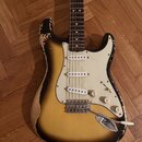Elektrická kytara typu Stratocaster s barevným přechodem od žluté k černé. Instrument vykazuje výrazné opotřebení laku, zejména na okrajích korpusu a…