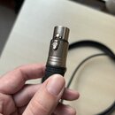 Detailní pohled na konektor kabelu v ruce. Kovová část konektoru nese vyražené logo ve tvaru stylizovaného písmene P v kruhu a černý plastový kryt má…