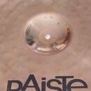 Kruhový mosazný činel s kovaným povrchem a vyvýšeným středem. V dolní části je černý nápis pAiste a pod ním menší text MADE IN SWITZERLAND. Povrch vy…