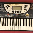 Černý digitální klavír značky YAMAHA, model PSR-270. Nástroj má standardní klávesnici a ovládací panel s displejem, tlačítky pro výběr stylů a hlasů…