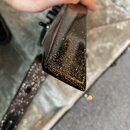 Detailní pohled na hranu černého hudebního nástroje s lesklým povrchem. Povrch je voorzien hustým zlatavým třpytivým efektem. Na fotografii nejsou žá…