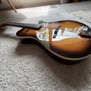 Akustická kytara s korpusem v barevném přechodu od žluté přes hnědou k černé (sunburst). Nástroj leží na světlém koberci a má tmavý hmatník s kovovým…