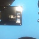 Detail zadní strany modré elektrokytary s černým plastovým krytem elektroniky. Pod krytem je vidět přepínač s nápisem "LTD" a potenciometr. Na modrém…