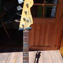 Fotografie zachycuje hlavu a část hmatníku elektrické basové kytary v přírodní dřevěné barvě. Na hlavě jsou vidět nápisy Squier, Jazz BASS a Fender.…
