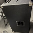 Černý basový nebo kytarový kombozesilovač s povrchem z texturovaného vinylu. Horní panel obsahuje ovládací knoflíky a černou přenosnou rukojeť s kovo…