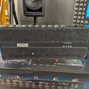 Zadní strana černého komba s texturovaným povrchem a dvěma vodorovnými mřížkami. V horní části je řada konektorů s popisky: VOLUME (SPEAKERS), EXP 1/…