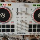 Bílý DJ kontrolér s dvěma černými jog-koly s červeným podsvícením. Na spodní hraně je nápis Numark MIXTRAK PRO II. Zařízení obsahuje fadery, knoflíky…