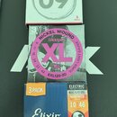 Tři balení strun pro elektrickou kytaru položená na sobě. Horní bílé balení značky Fender s nápisy 09, ELECTRIC GUITAR a SUPER 250 XL NICKEL-PLATED S…