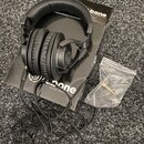 Černá uzavřená sluchátka s polstrováním z umělé kůže leží na černé krabici. Na krabici je bílý nápis bone audio experience a logo. K sluchátkům je př…