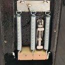 Fotografie zachycuje vnitřní část vyfrézovaného prostoru v černém trupu kytary. V prostoru jsou umístěny tři kovové pružiny tremola a kovový mechanis…