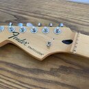 Fotografie zachycuje hlavu elektrické kytary z přírodního světlého dřeva. Na povrchu je černý nápis Fender® STRATOCASTER® a v horní části nápis ORIGI…
