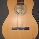 Akustická kytara s přírodním dřevěným povrchem korpusu a tmavým hmatníkem. Uvnitř otvoru rezonanční desky je vidět štítek s nápisem Fender ACOUSTICS…