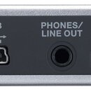 Záběr na zadní stranu stříbrného elektronického zařízení s černým panelem konektorů. Na panelu jsou nápisy DC IN, USB, PHONES/LINE OUT a VOLUME s dop…