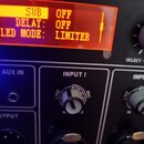 Detailní záběr na ovládací panel elektronického zařízení. Oranžový displej zobrazuje texty SUB: OFF, DELAY: OFF a LED MODE: LIMITER. Pod displejem js…