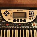 Černý digitální klavír značky YAMAHA, model PSR-270. Na ovládacím panelu jsou vidět různé tlačítka, posuvníky a nápisy jako FUNCTION, SONG, STYLE, VO…
