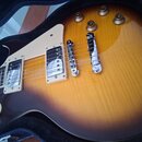 Elektrická kytara typu Les Paul s barevným přechodem od žluté k tmavě hnědé (sunburst). Nástroj má dva humbuckery s krémovými rámečky, chromovaný kob…