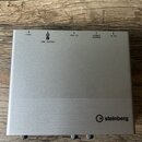 Stříbrné audio rozhraní značky steinberg s matným kovovým povrchem. V horní části jsou nápisy +48V, R L LINE OUTPUT, USB 2.0, POWER SOURCE a 5V DC. V…