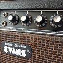 Detailní pohled na ovládací panel a přední část kytarového komba. Na černém panelu jsou umístěny ovládací knoflíky s nápisy VOLUME, MASTER, BASS a MI…