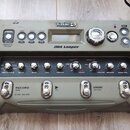 Šedý looper Line 6 JM4 Looper s kovovými ovládacími prvky. Na horním panelu jsou tlačítka GUITAR, DRUMS, INPUTS, SETTINGS, MIC/AUX, SONG, LEVEL a TON…