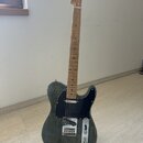 Elektrická kytara typu Telecaster s tmavě šedým trupem s viditnou strukturou dřeva a černým pickguardem. Hmatník a hlava jsou vyrobeny ze světlého dř…