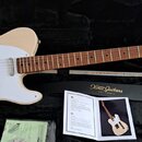 Elektrická kytara typu Telecaster v přírodní dřevěné barvě s bílým pickguardem, umístěná v černém tvrdém kufru. Na hlavě hmatníku je nápis Xotic guit…