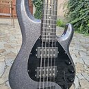 Elektrická basová kytara s trpyhlivým šedým povrchem korpusu a černým pickguardem. Nástroj má dva snímače typu humbucker a tři černé ovládací knoflík…