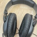 Černá nadušnice s kabelovými připojeními. Sluchátka mají černé polstrování na hlavovém oblouku i na mušlích, které vykazuje známky opotřebení a vrásn…