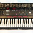 Černý digitální klavír s bílými a černými klávesami. Na ovládacím panelu je nápis YAMAHA PSS-590 a logo AWM. Přístroj obsahuje červené digitální disp…