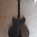 Zadní strana polodubové elektrické kytary v černé barvě s lesklým povrchem. Na hlavě jsou vidět zlaté ladičky a nápis "Epiphone". Tělo kytary má vyve…