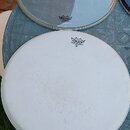 Dvě bubenové kožehy značky REMO položené na kulatém stole. Horní koža je průhledná s nápisy REMO a SONOR, spodní koža je bílá, matná a nese nápis REM…