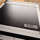 Černý transportní kufr s hliníkovými hranami a vrchními lištami. V pravém dolním rohu je připevněn kovový štítek s nápisem FLIGHT PRO a textem INNOVA…