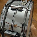 Stříbrný, chromovaný malý buben s kovovým korpusem. Na horním obruči je vidět kulatý štítek s nápisem "LUDWIG" a pod ním menší text "Standard". Povrc…