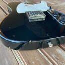 Černá elektrická kytara typu Telecaster s jedním snímačem a dvěma ovládacími knoflíky. Na hraně korpusu jsou vidět výrazné odřasení laku a známky opo…