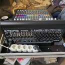 Zadní strana černého digitálního mixážního pultu s nápisem MIDAS M32R. Jsou vidět početné vstupy a výstupy typu XLR, jack a konektory pro Ethernet a…